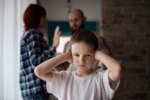 girl covering her ears while parents argue